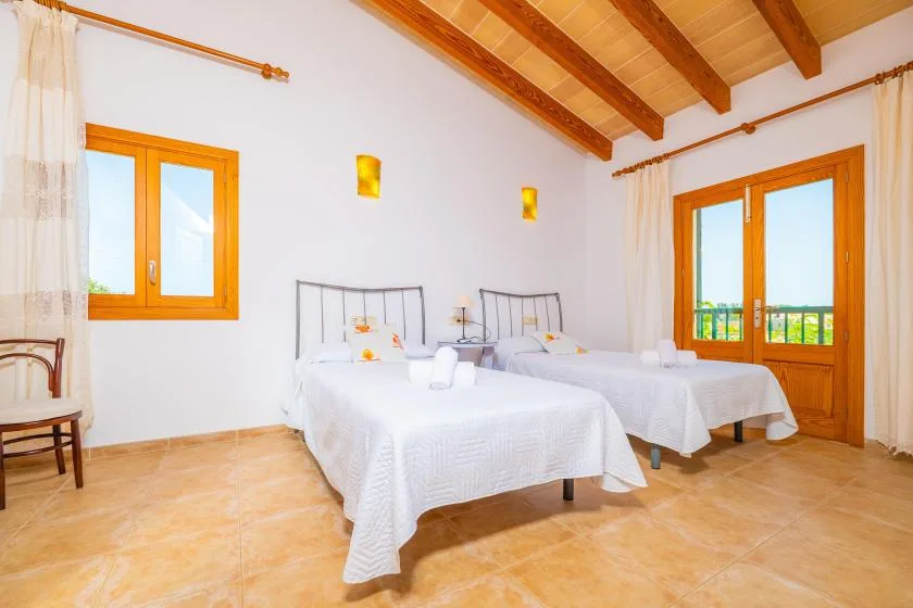A bright bedroom with two beds and exposed wooden ceiling beams.
