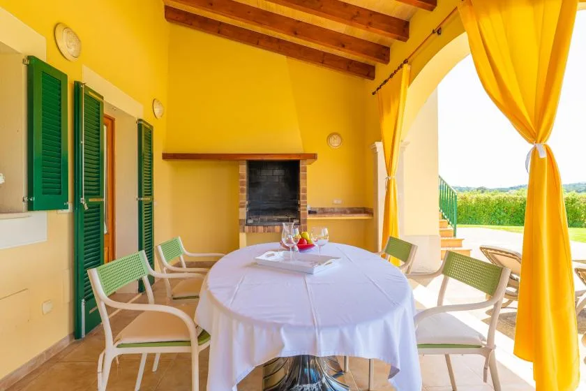 A bright dining area with a round table and green shutters opens onto a terrace.