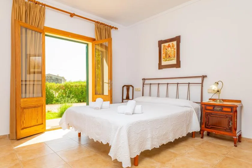 A bedroom with a neatly made bed beside open wooden doors leading to a garden.