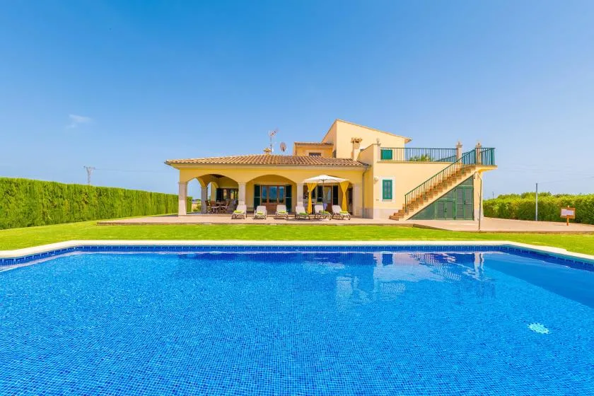 A swimming pool sits in front of a house with a covered patio.