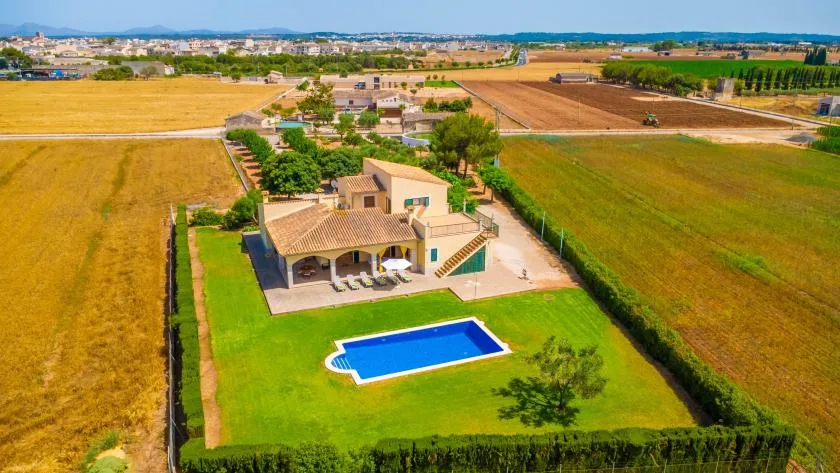 An aerial view of a house with a swimming pool amid open fields.