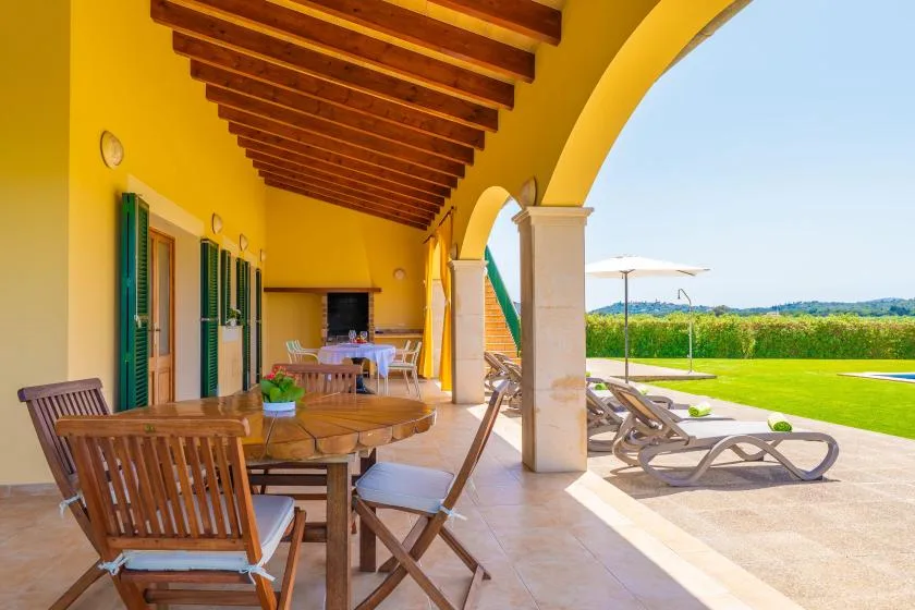 A covered outdoor dining area opens onto a lawn and swimming pool.