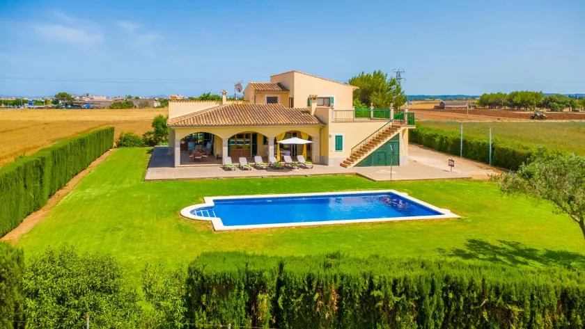 A house and swimming pool sit in a green lawn surrounded by hedges.