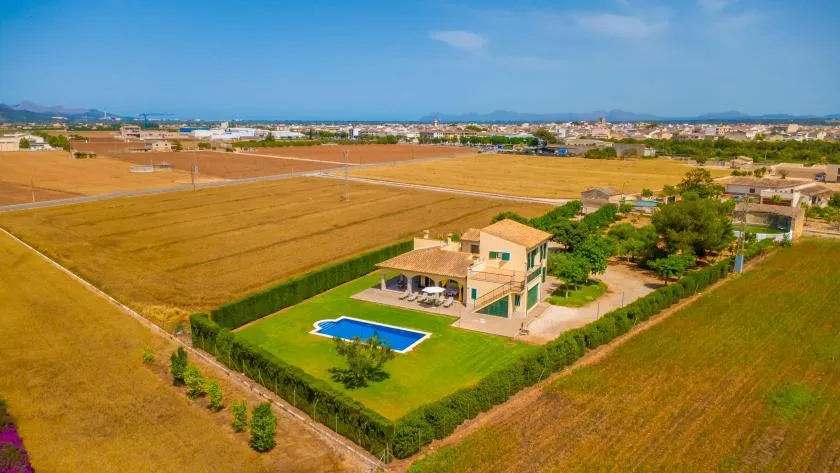 Aerial view of a house with a blue swimming pool amid open fields.
