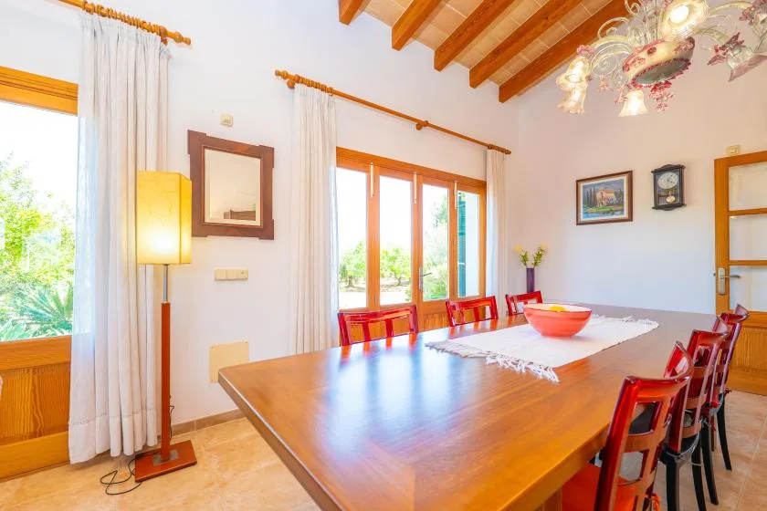 A dining room with a long wooden table and chairs beneath exposed ceiling beams.