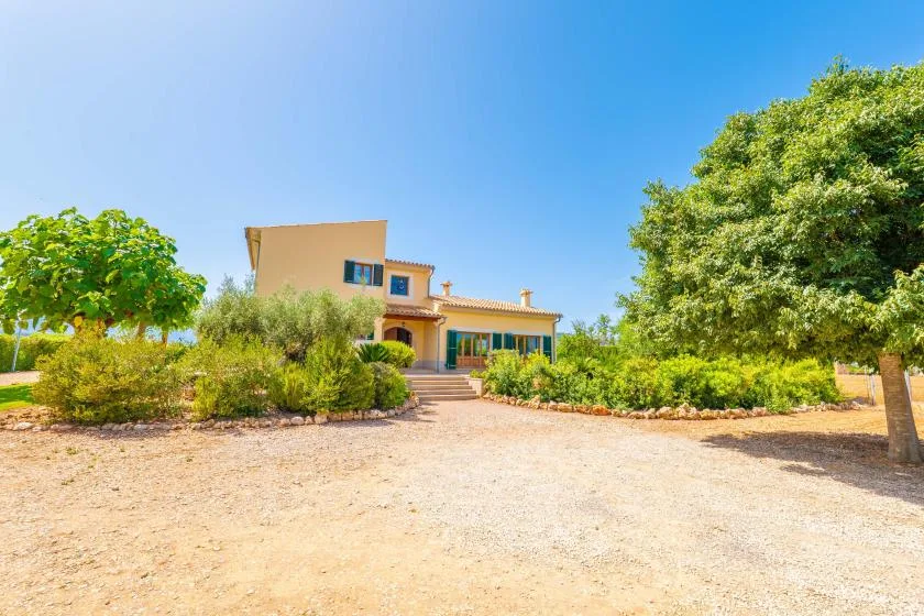 A house stands beyond a landscaped garden and broad gravel drive.