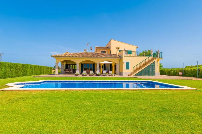 A two-story house with a covered patio stands behind a swimming pool and lawn.
