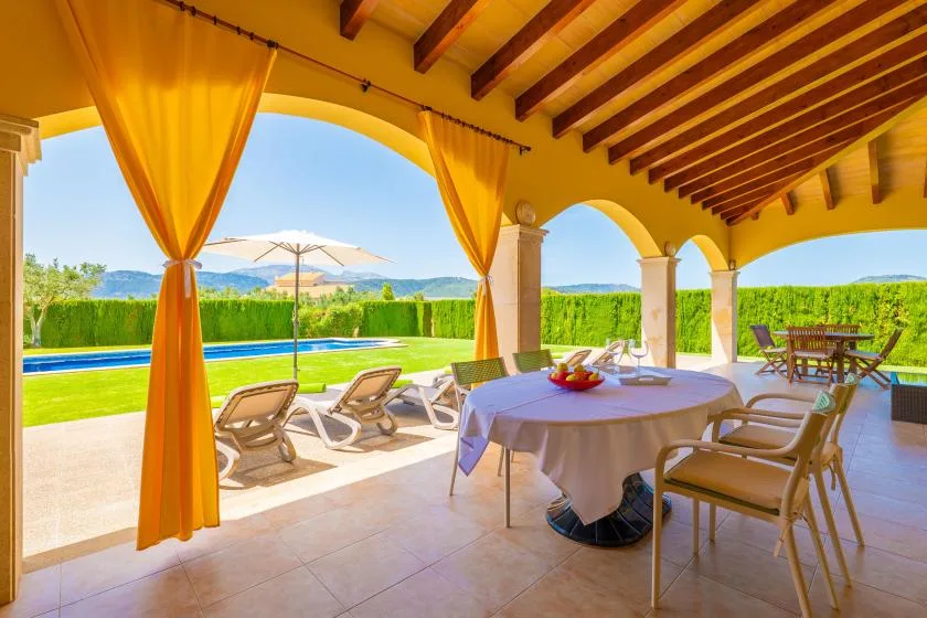 A covered outdoor dining area with a table overlooking a pool and garden.