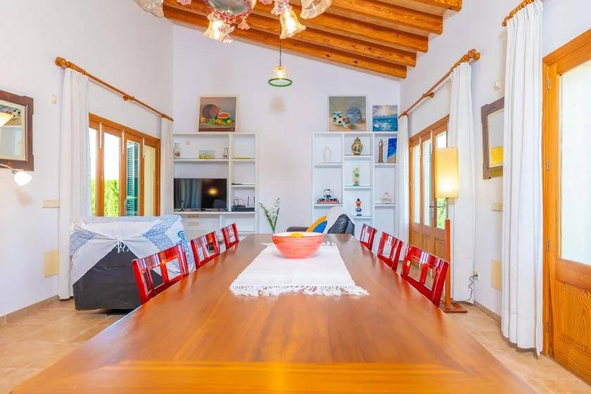 A dining room with a long wooden table and red chairs.