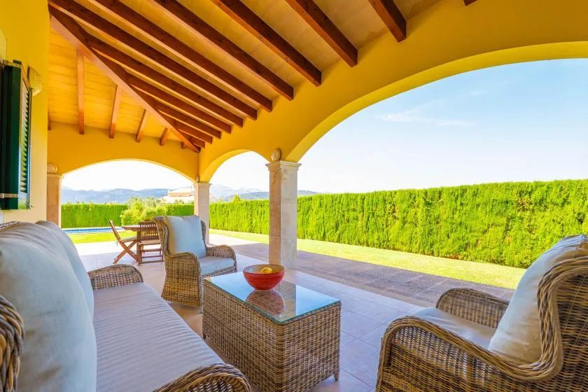 A covered outdoor seating area overlooks a green hedge and distant hills.