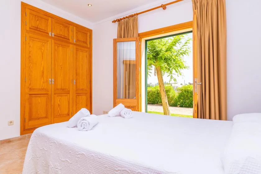 A bedroom with a large bed, wooden wardrobe, and an open window overlooking greenery.