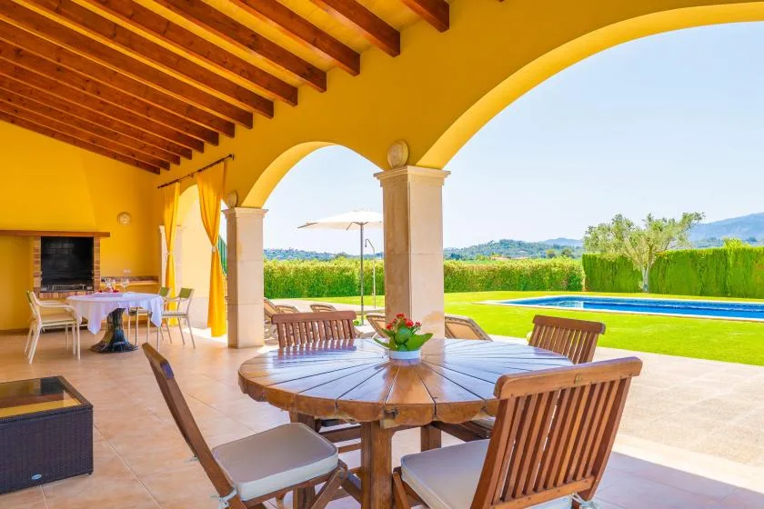 A covered outdoor dining area opens onto a lawn and distant countryside.