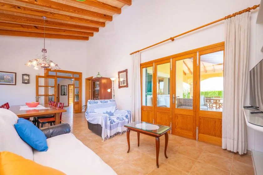 A bright living and dining area has seating, a small table, and wooden-framed glass doors.