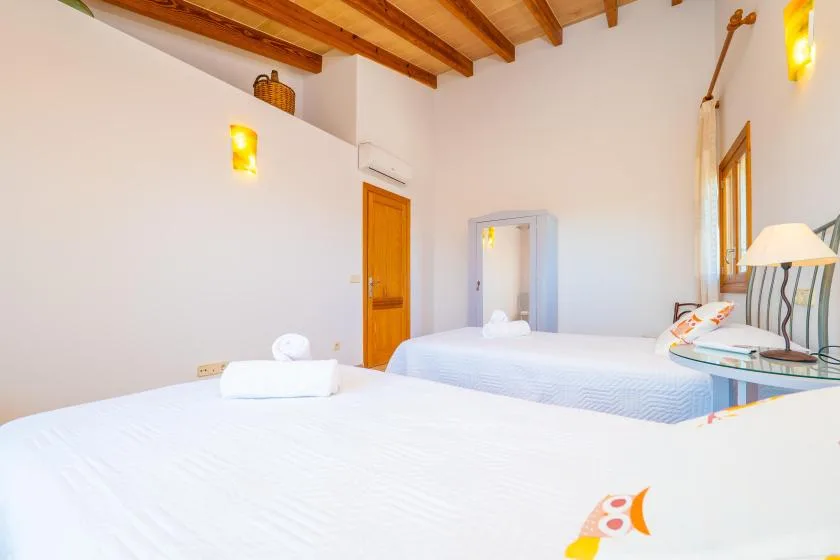 A bright bedroom with two beds, wooden ceiling beams, and a window.