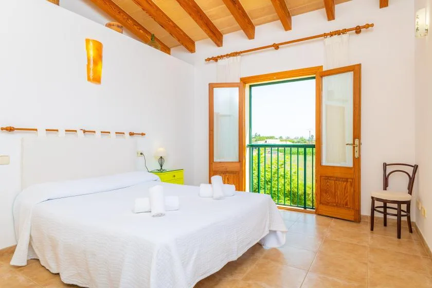 A bright bedroom with a bed beside open wooden doors leading to a small balcony.