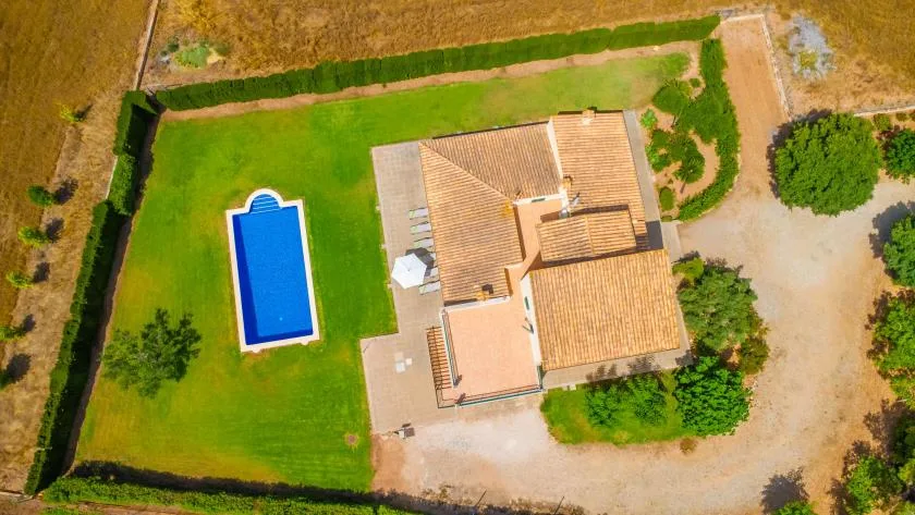 An aerial view of a house surrounded by a green lawn, with a swimming pool.