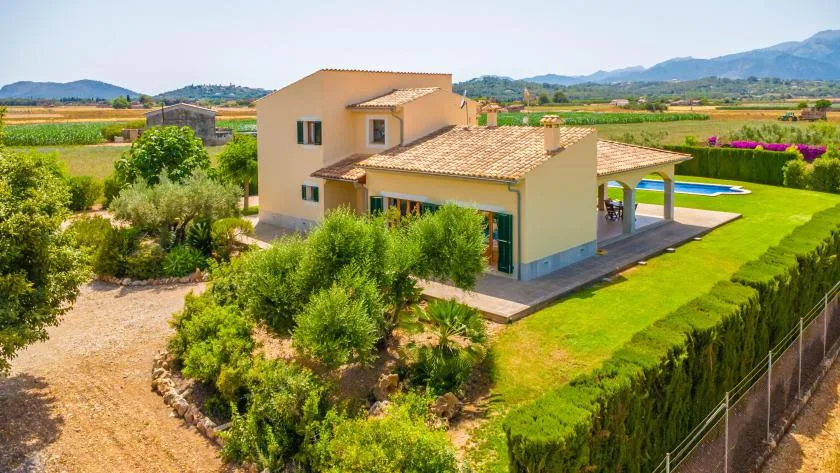 A Mediterranean-style house sits beside a landscaped lawn and swimming pool.