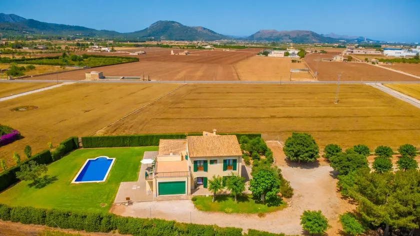 Aerial view of a house beside fields, with mountains in the distance.