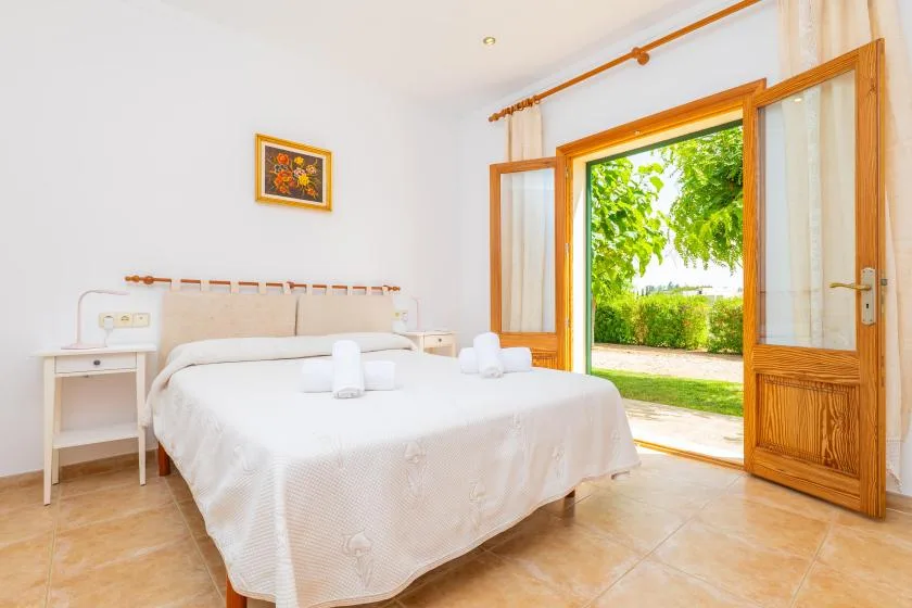 A bedroom with a double bed and open wooden doors leading to a garden.