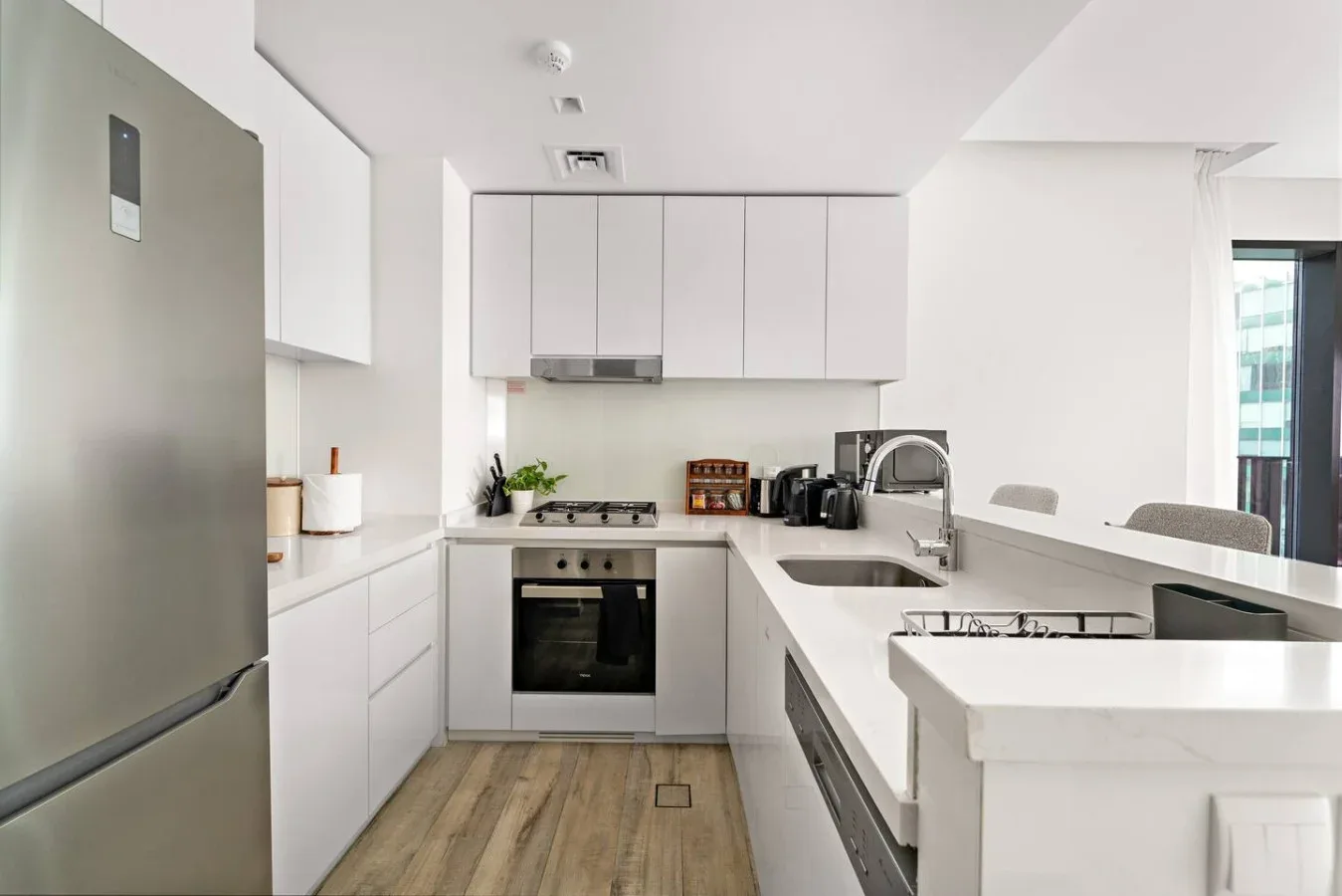 Una cocina moderna y luminosa con gabinetes blancos, electrodomésticos de acero inoxidable y una barra.