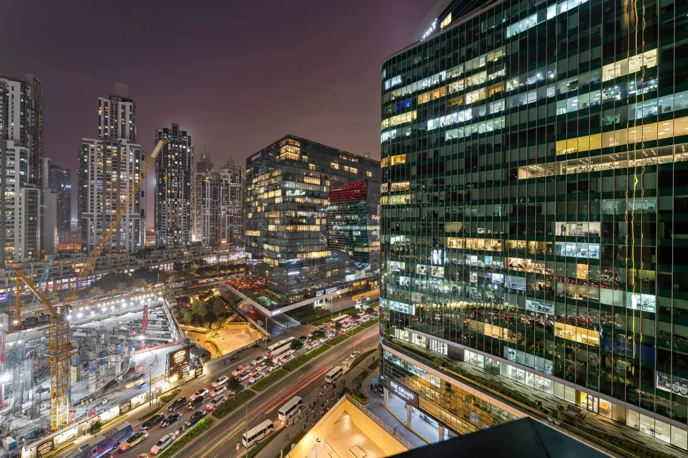 Un paisaje urbano nocturno muestra torres de oficinas iluminadas y calles concurridas.