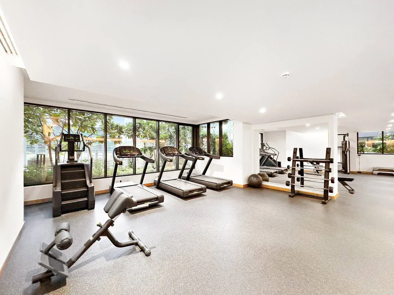 Un gimnasio luminoso con cintas de correr, equipo de pesas y grandes ventanas.