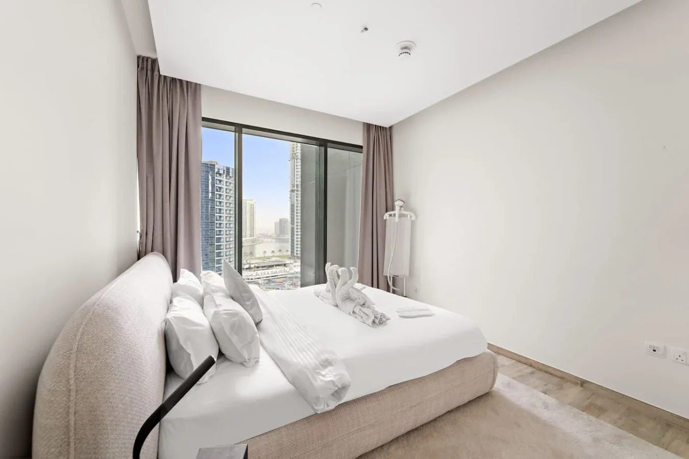 Un dormitorio luminoso con una cama bien tendida junto a una ventana grande.