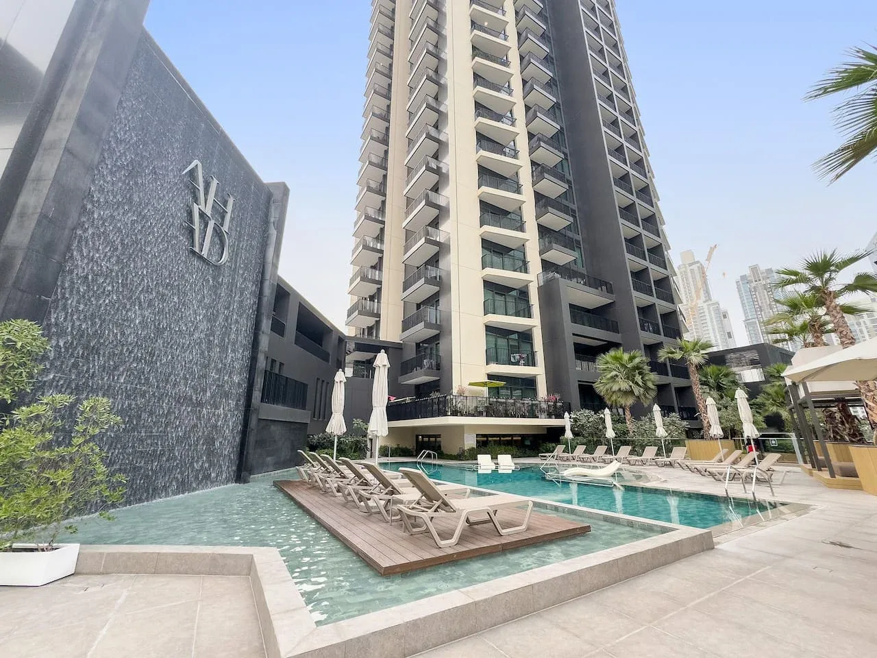 Un edificio alto da a una piscina exterior con asientos para descansar.