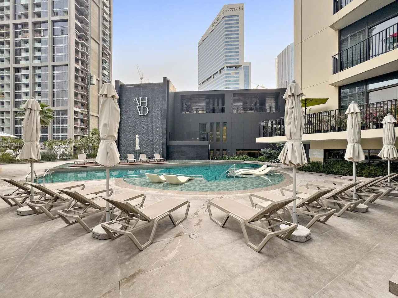 Una zona de piscina en la azotea con asientos y edificios altos alrededor.