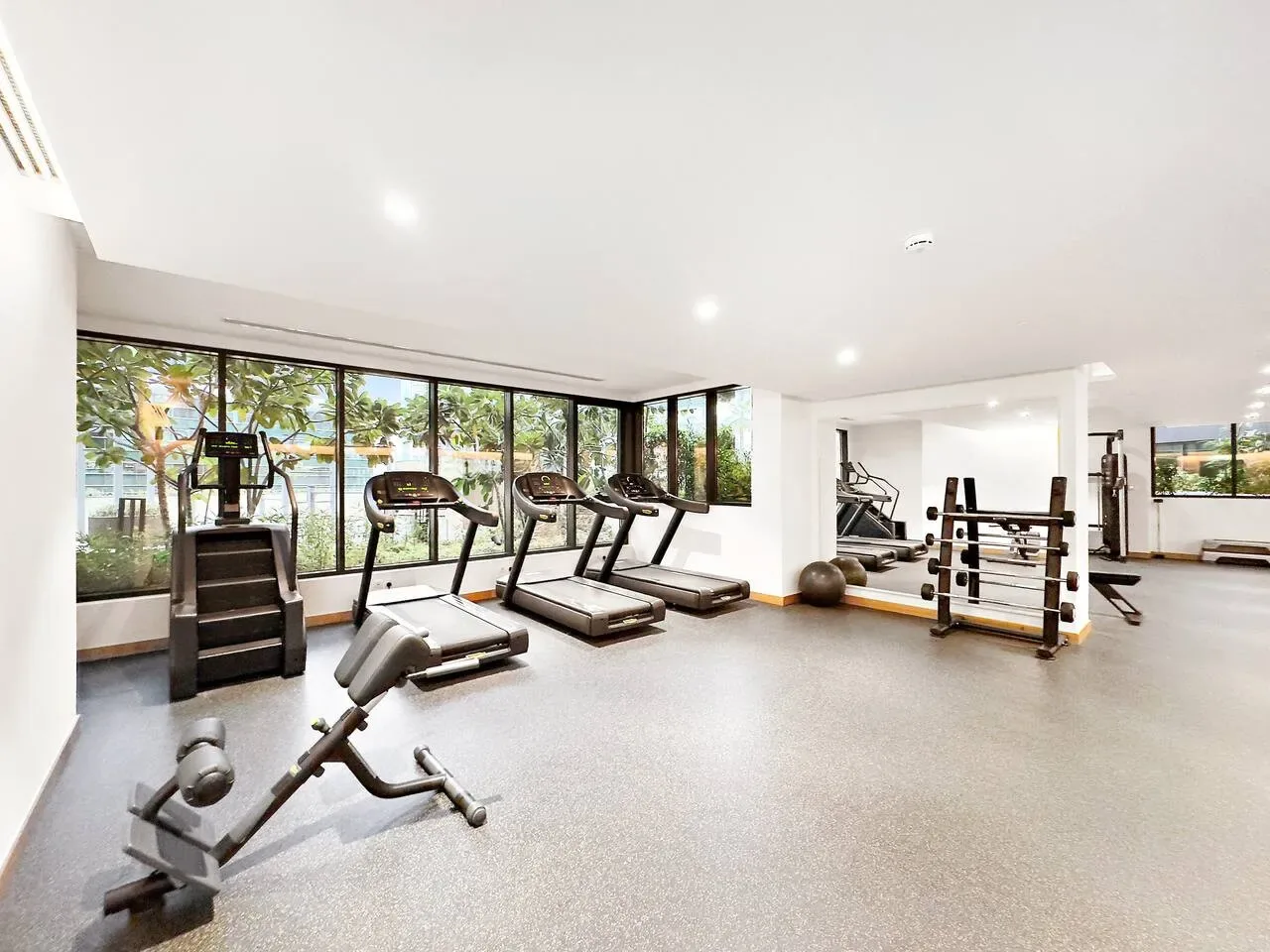 Un gimnasio luminoso con cintas de correr, pesas y grandes ventanas.