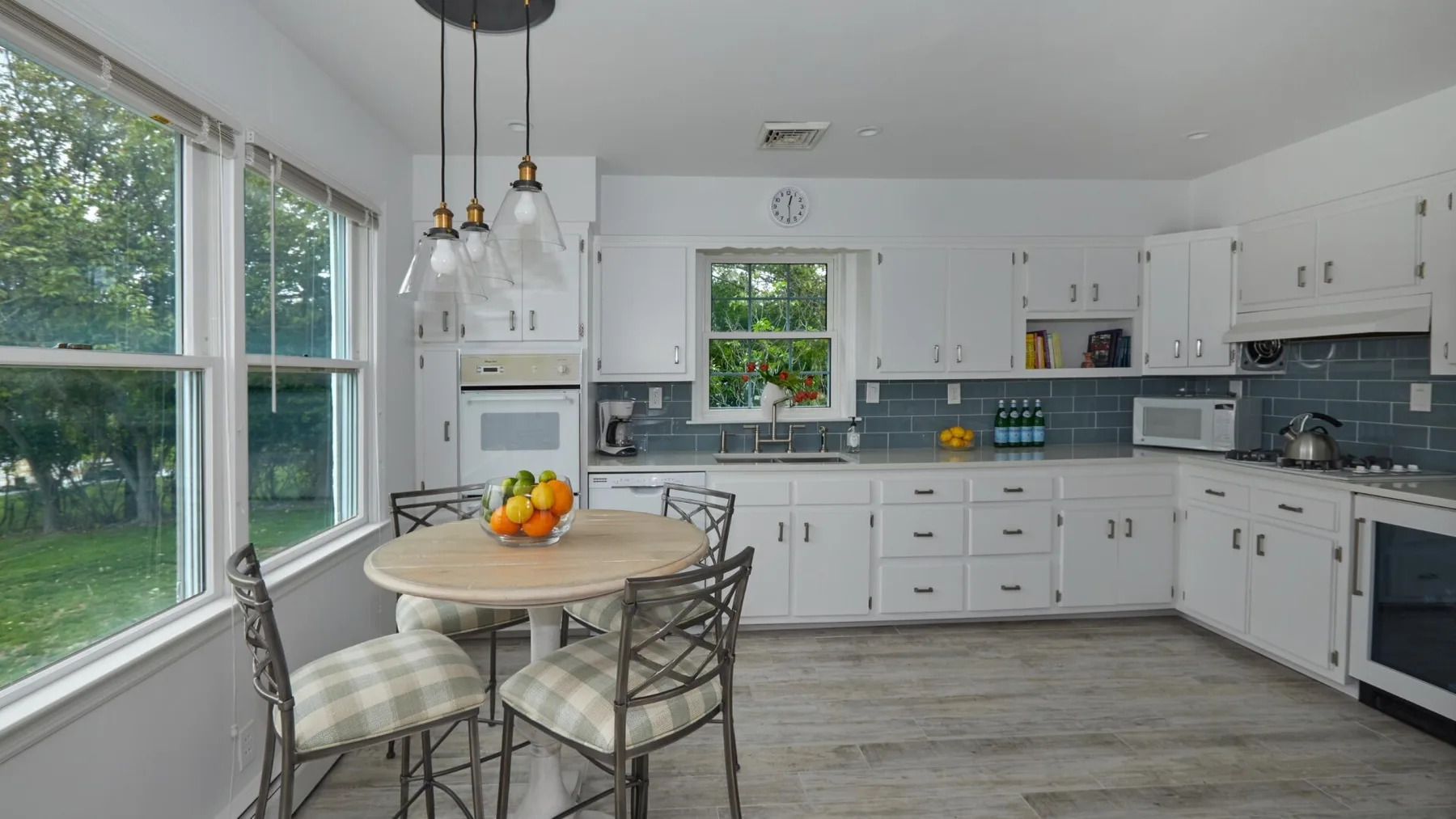 Una cocina luminosa con gabinetes blancos, una mesa de comedor y grandes ventanas.