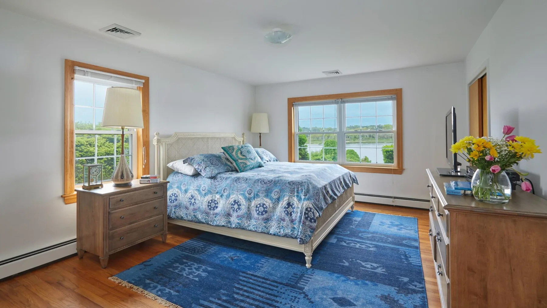 Un dormitorio luminoso con una cama junto a dos ventanas grandes.
