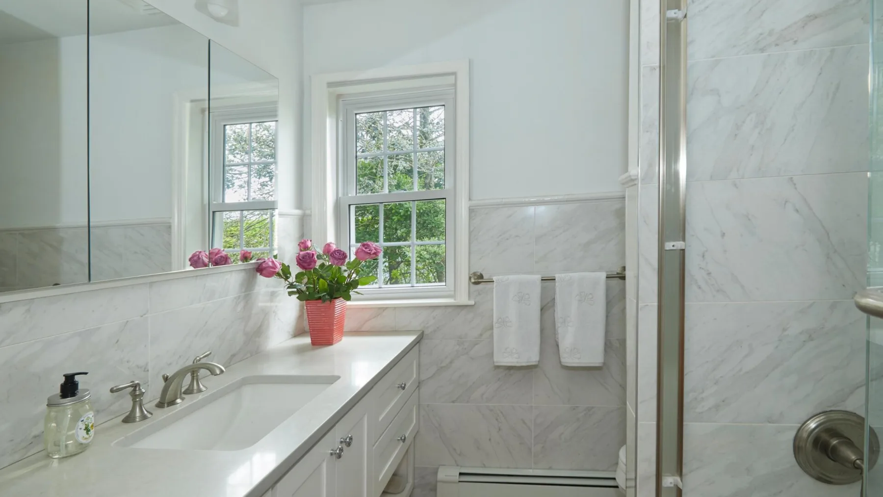 Un baño luminoso con lavabo, espejo de pared y una ventana con vista a vegetación.