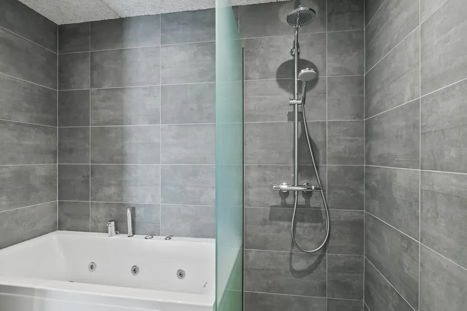 Un baño alicatado con una bañera blanca y una ducha fijada a la pared.