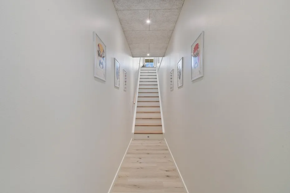 Un pasillo estrecho conduce a una escalera, con cuadros enmarcados en las paredes.