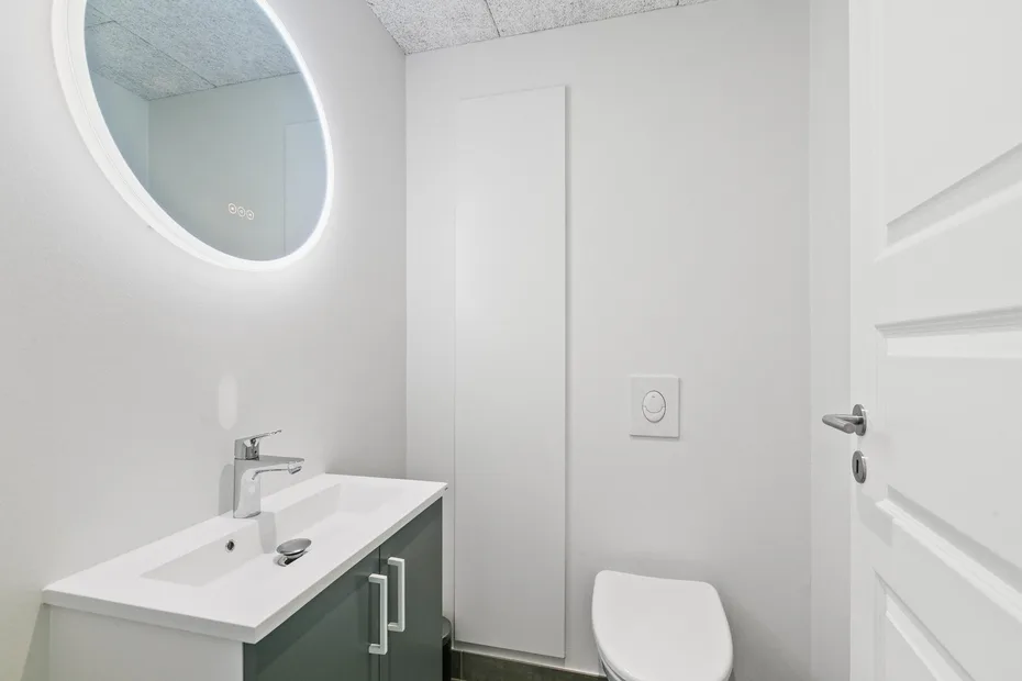 Un baño luminoso con lavabo, espejo ovalado e inodoro.