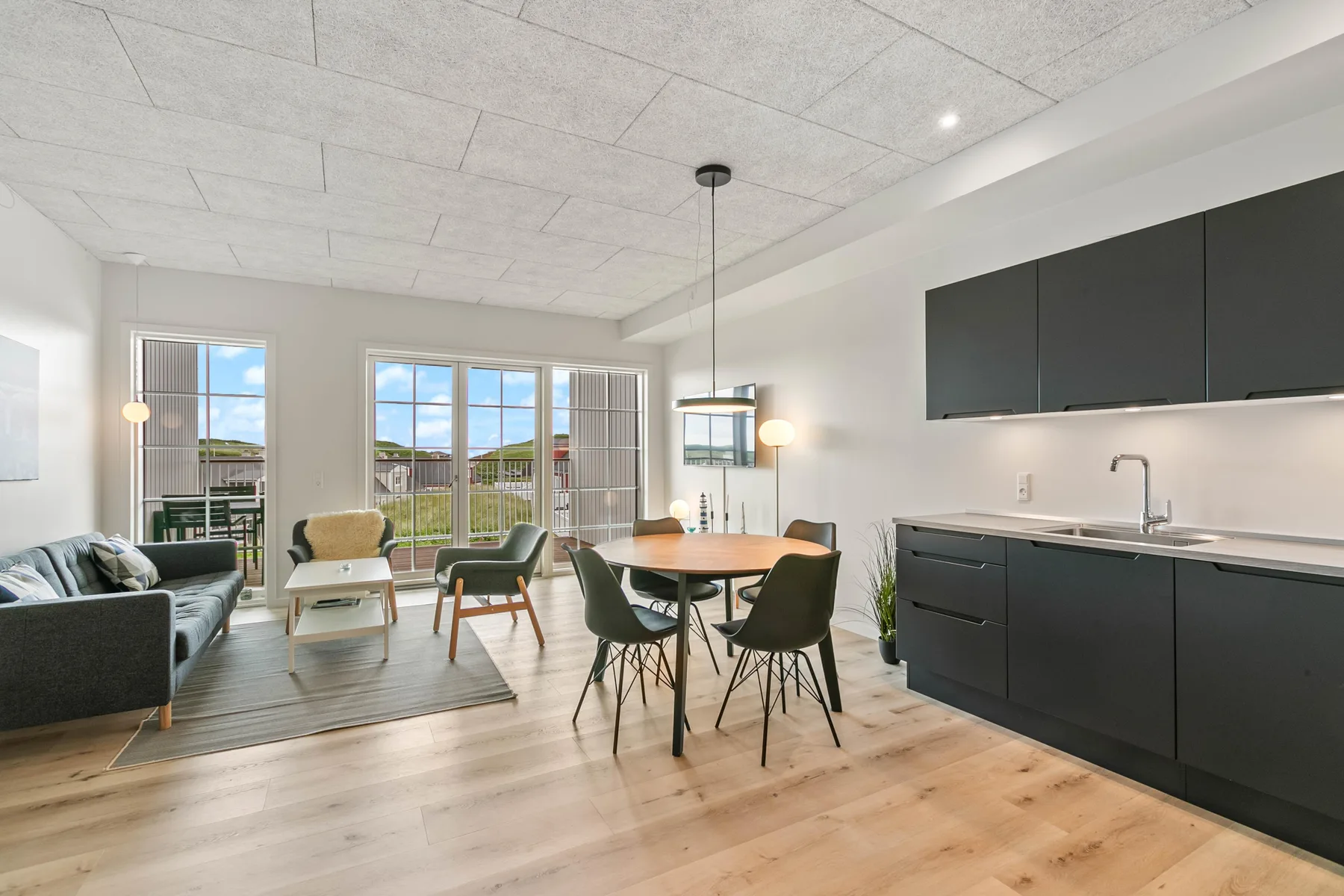 Sala de estar y comedor de planta abierta con cocina y ventanales.