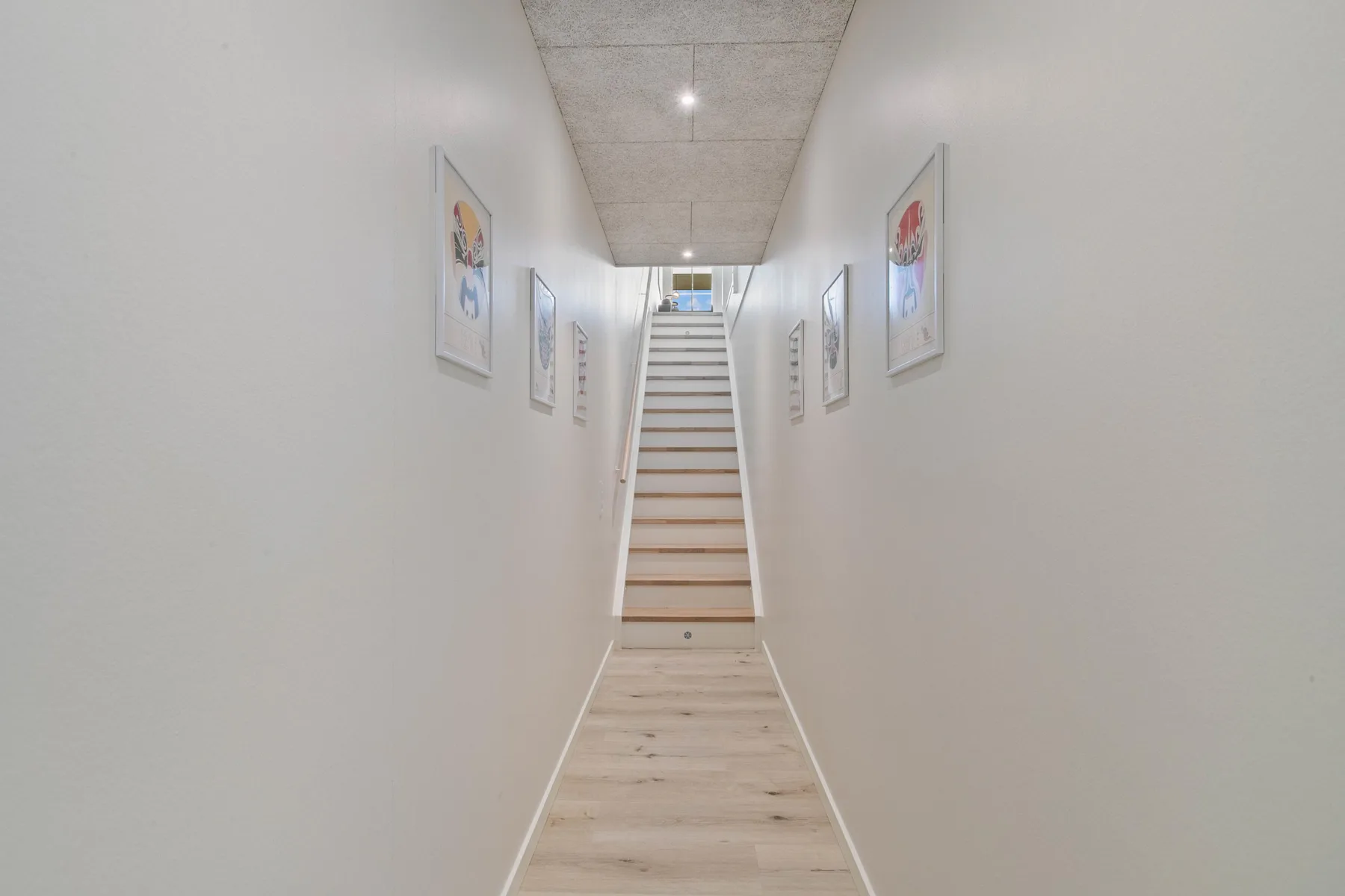 Un pasillo luminoso con cuadros enmarcados conduce a una escalera.