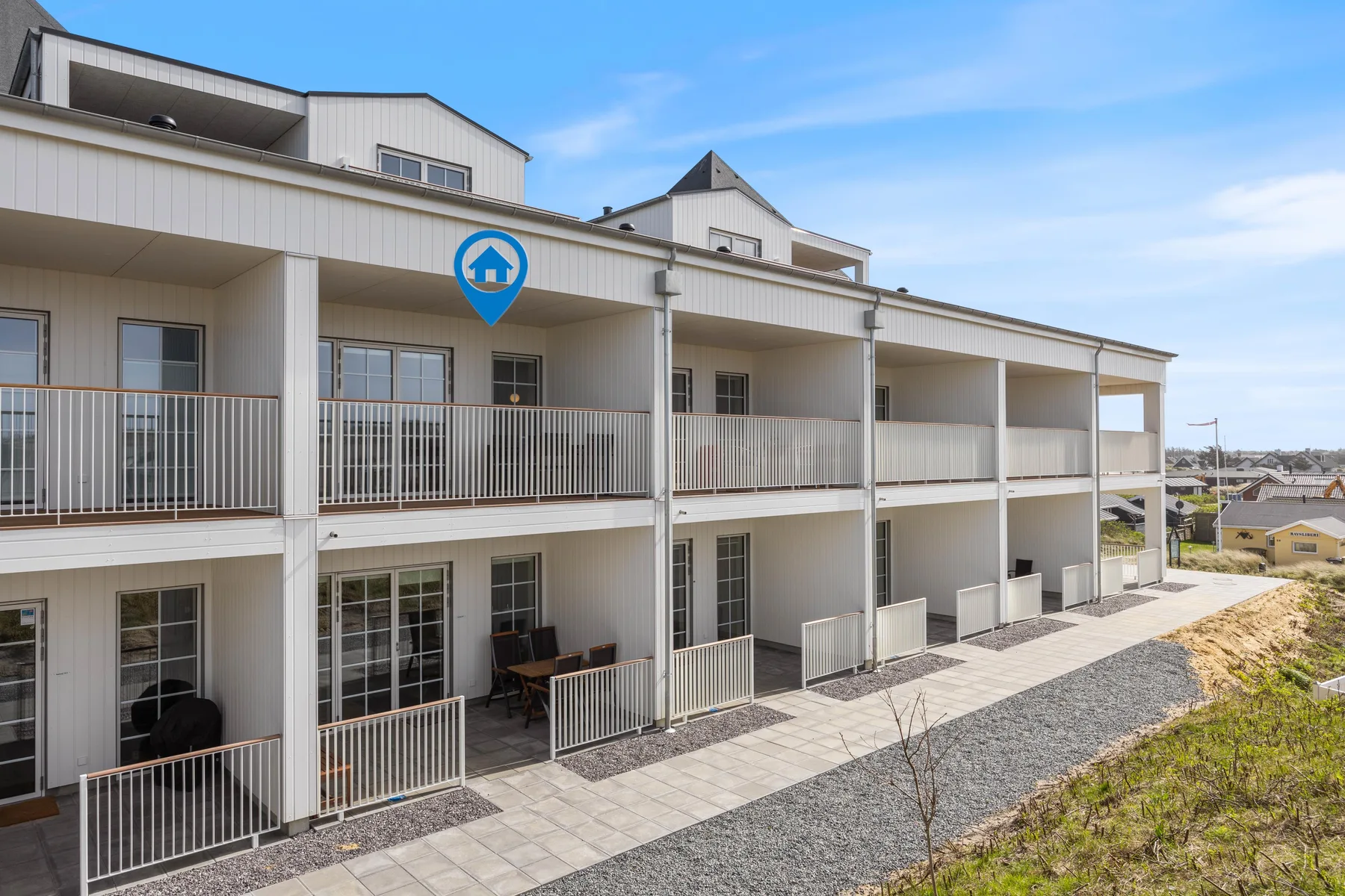 Un moderno edificio de apartamentos con balcones junto a un camino pavimentado.