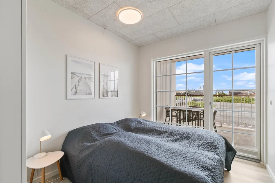 Un dormitorio con una cama junto a grandes ventanas y una pequeña mesa de comedor.