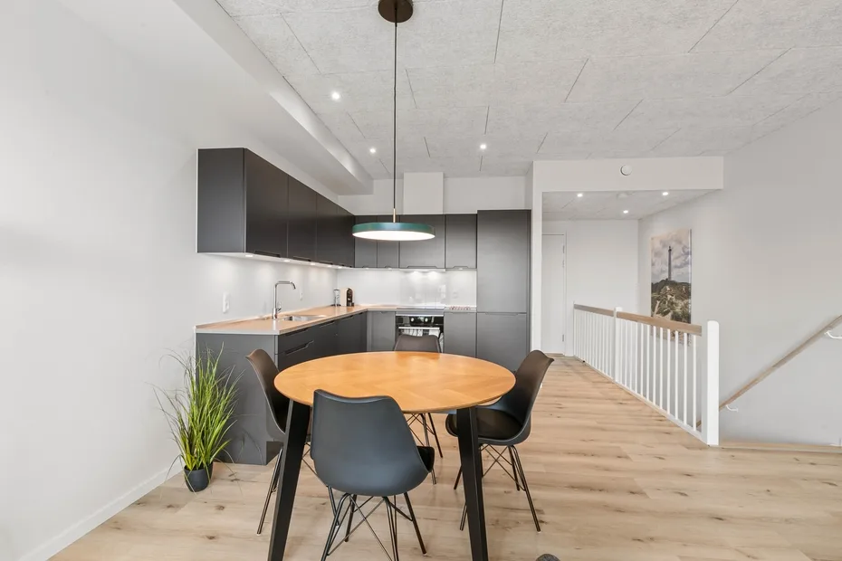 Cocina y comedor de planta abierta con una mesa de madera y armarios oscuros.