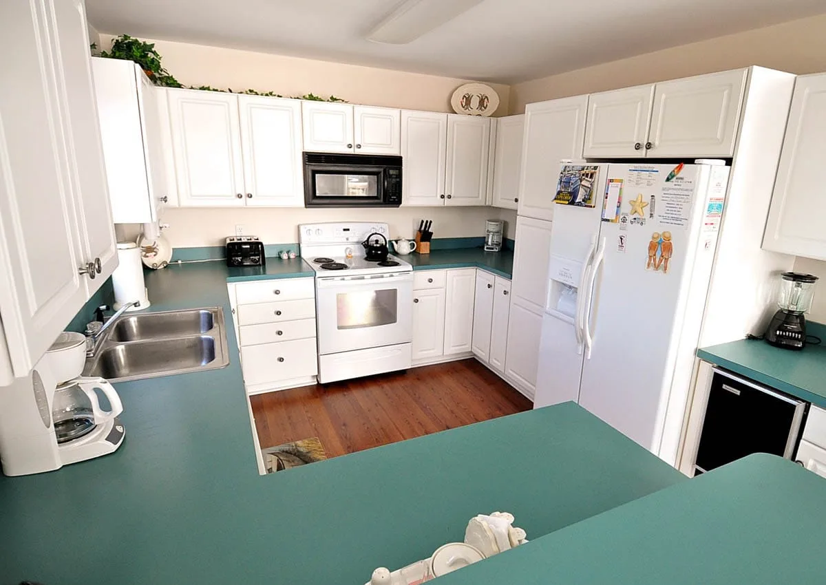 A bright kitchen with white cabinets, teal countertops, and a central cooking area.