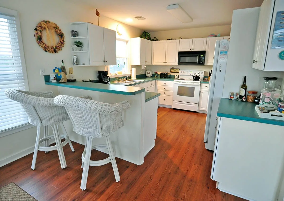 A bright kitchen with white cabinets, teal counters, and a breakfast bar.