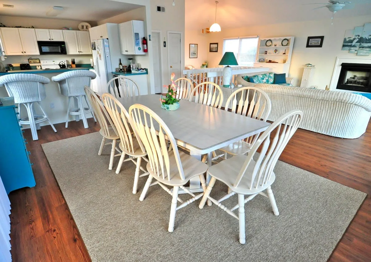 A dining area with a long table and chairs beside an open kitchen and living room.