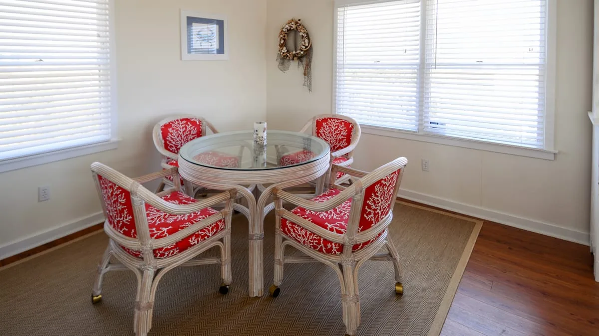 A bright dining nook with a round glass table and red patterned seating.