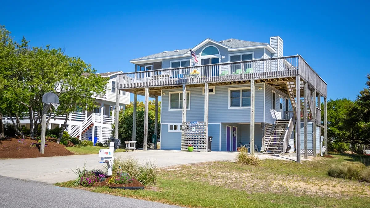A raised coastal-style house with a broad deck and exterior stairs.