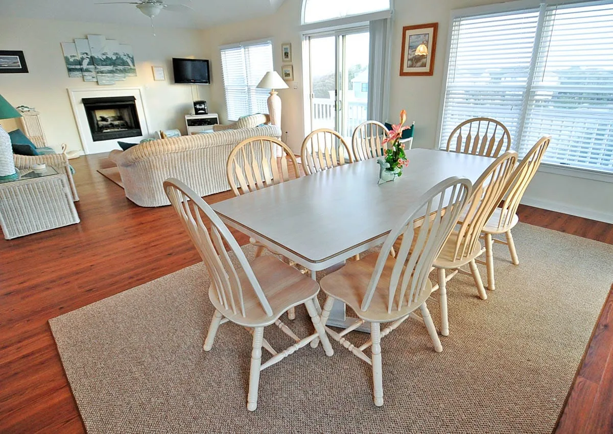 A bright dining area with a long table and a living room beyond.