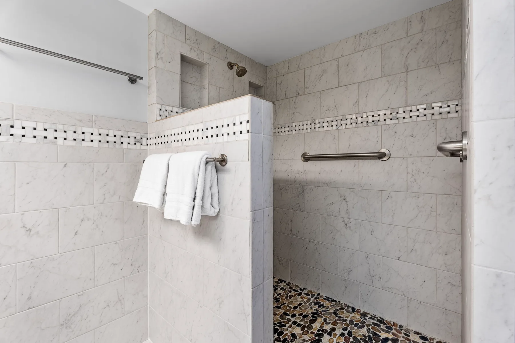 Una zona de ducha alicatada con suelo de diseño de guijarros y toallas colgadas cerca.