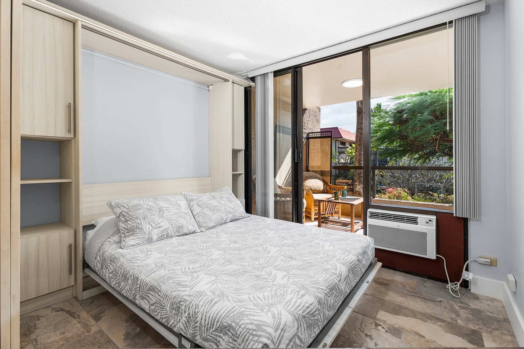 Un dormitorio con una cama junto a grandes puertas corredizas de vidrio con vista a la vegetación.