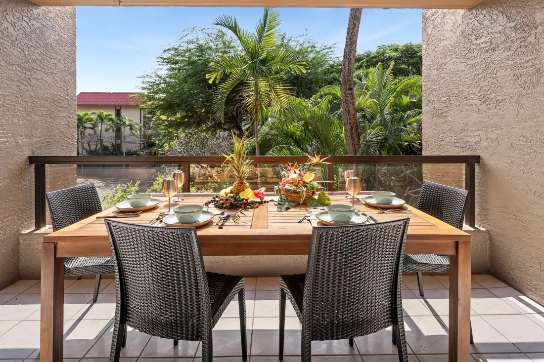 Comedor en un patio con la mesa puesta y vistas a palmeras y vegetación.